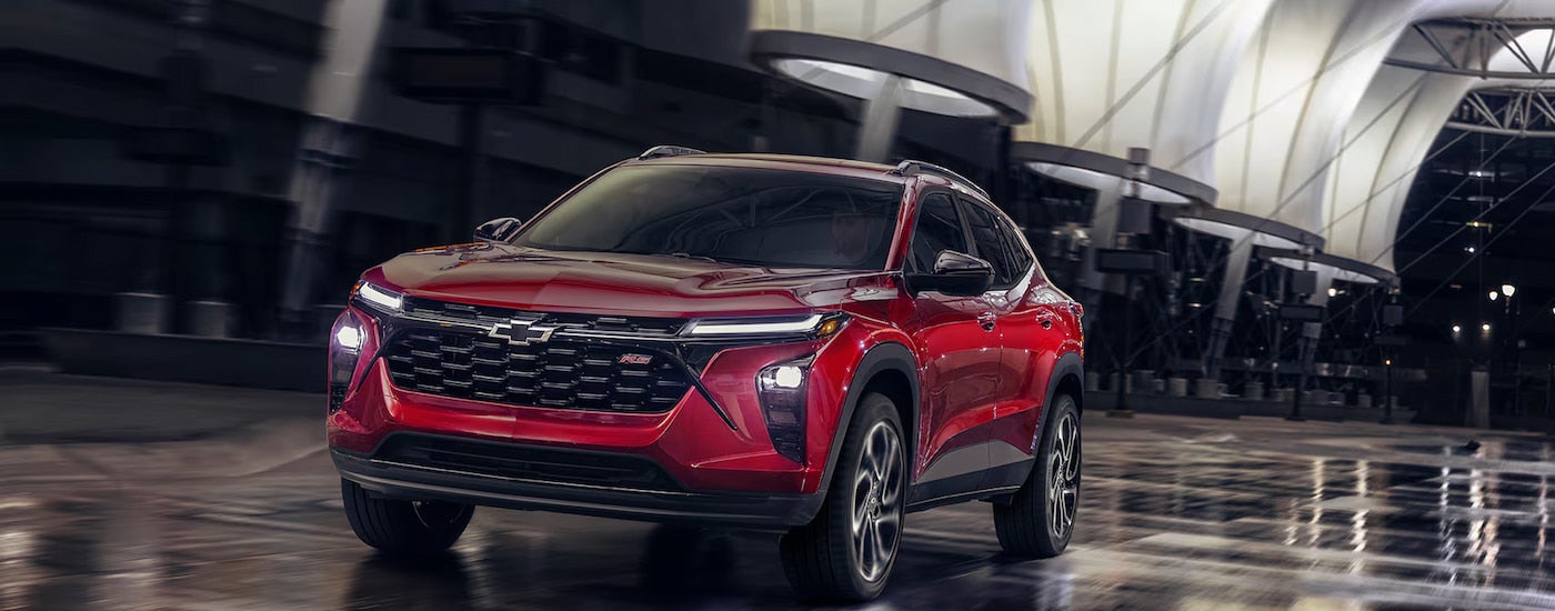 A red 2025 Chevy Trax driving in a city at night