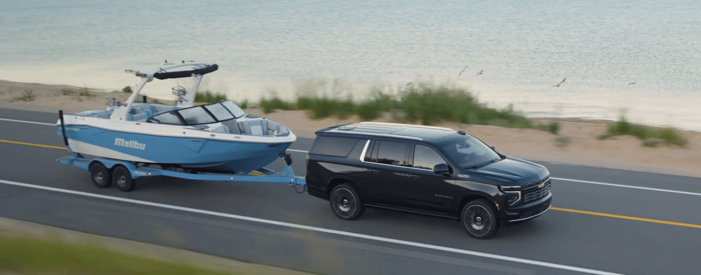 Black 2026 Chevy Suburban towing a boat past a body of water
