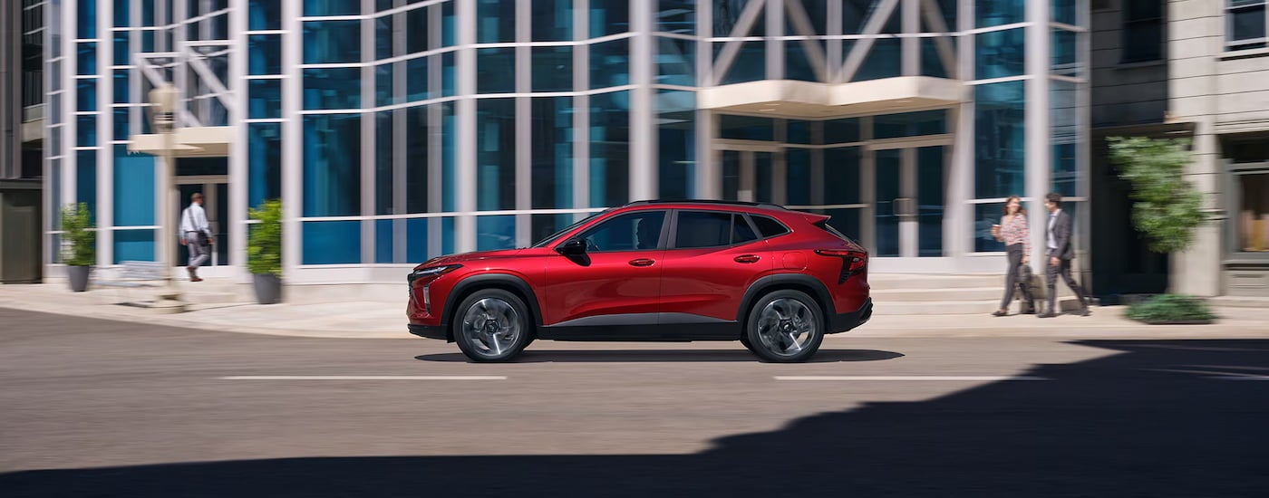 Side of a red 2025 Chevy Trax RS driving down a city street.